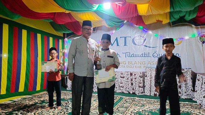 Keuchik Gampong Blang Asan, H Aidil Sutrisno saat menyerahkan piala juara MTQ tingkat gampong setempat, Minggu (3/12/2023).