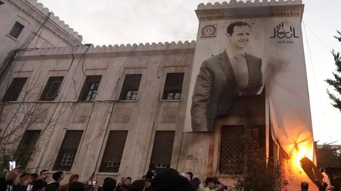 Warga di Hama membakar spanduk besar bergambar Presiden Suriah Bashar al-Assad yang tergantung di fasad gedung pemerintah kota pada tanggal 5 Desember 2024, setelah faksi oposisi bersenjata menguasai kota di wilayah barat-tengah Suriah tersebut.