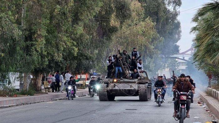 Orang-orang mengendarai tank di kota Daraa, Suriah selatan, pada tanggal 7 Desember setelah runtuhnya pasukan pemerintah.