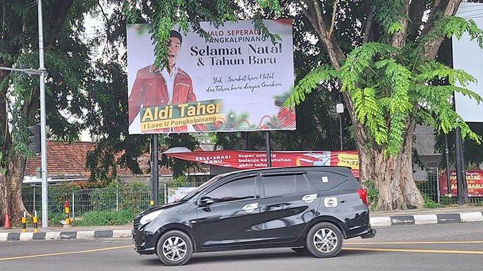 Kendaraan roda 4 saat melintas di depan beliho bergambar Aldi Taher yang terpasang di Simpang lampu merah Tranasmart, Kota Pangkalpinang pada Kamis (26/12/2024).