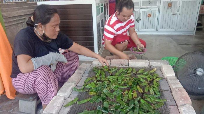 Tampak Riri pegawai otak-otak Asam sibuk membolak-balikan otak-otak yang sedang dipanggang di atas bara api, sementara Iwan (baju merah putih) pemilik warung menyiapkan hidangan konsumen, Minggu (24/10/2021)