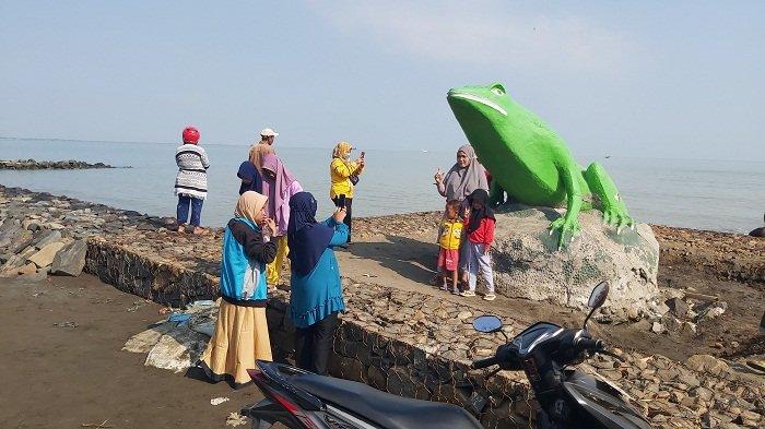 Pengunjung berfoto di patung katak yang menjadi ikon Pantai Pulo Kodok Kota Tegal, Minggu (10/9/2023). Pantai yang bersih dan dilengkapi tanggul laut membuat tingkat kunjungan wisatawan meningkat.