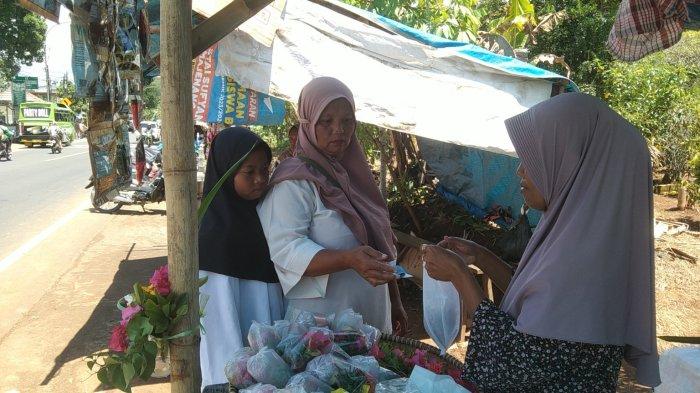 MELAYANI PEMBELI - Salah satu pedagang bunga setaman di kawasan Makam Ciguling, Kecamatan Majenang, Kabupaten Cilacap saat melayani pembeli bunga, Kamis (27/2/2025). Puluhan pedagang bunga setaman berjualan di sekitar makam menjelang ramadan.