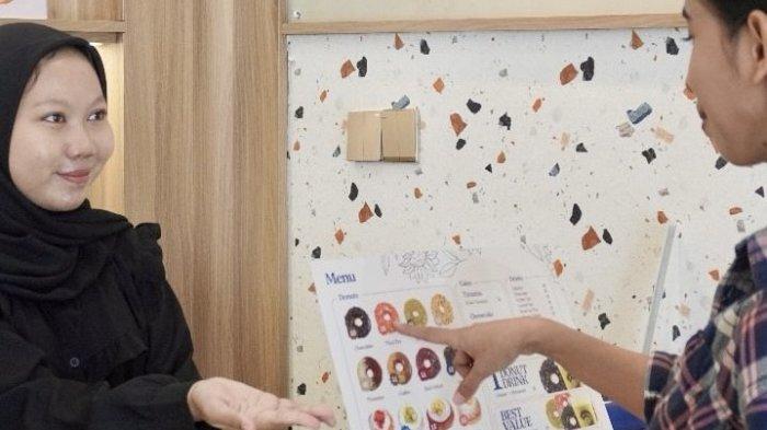 KULINER BOGOR - Seorang pengunjung tengah memilih varian donat di Doku Donat, didampingi oleh staf yang ramah. Doku Donat menawarkan beragam pilihan rasa unik yang membuat pengalaman berbelanja semakin menyenangkan.