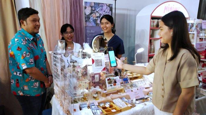 AVP of Merchant Acquisition - Business SME DOKU, Herunata Joseph (kiri) dan penyelenggara Diorama Art Market, Agnes Inke (tengah) menyaksikan pengunjung melakulan pembayaran digital menggunakan aplikasi DOKU dengan metode scan QRIS di stan Stellar Coronae pada acara bazar UMKM