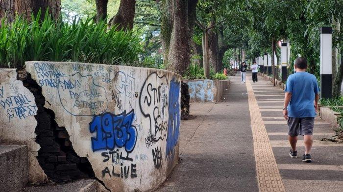 Warga melintas di samping tembok yang sudah retak dan dipenuhi coretan cat semprot, di Saparua Park, Kelurahan Citarum, Kecamatan Bandung Wetan, Kota Bandung, Jawa Barat, Sabtu (19/4/2025).