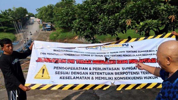 COPOT SPANDUK - Endang menunjukkan spanduk yang dipasang BBWS Citarum di jembatan perahunya, di Desa Anggadita, Klari, Karawang, Selasa (29/4/2025). Ia pun menyoroti nasib masyarakat bila jembatan tersebut ditutup.