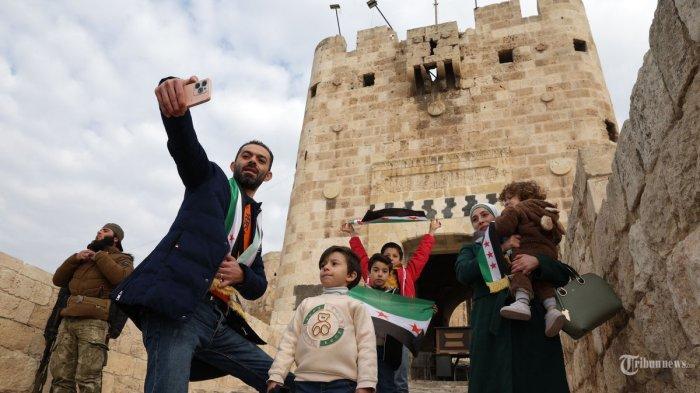 Satu keluarga Suriah difoto sambil kibarkan bendera revolusi di luar benteng bersejarah Aleppo pada tanggal 5 Desember 2024, saat pasukan antipemerintah, yang dipimpin oleh kelompok Islam Hayat Tahrir al-Sham (HTS), merebut kota Hama di wilayah tengah Suriah, beberapa hari setelah merebut pusat komersial negara itu.