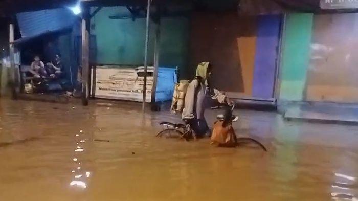 Seorang warga menerjang banjir sambil menuntun sepedanya di Kabupaten Cirebon.