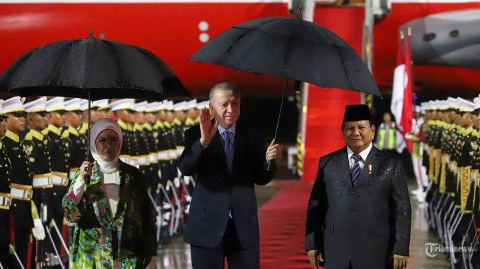 KEDATANGAN ERDOGAN - Presiden Turki Recep Tayyip Erdogan melambaikan tangan kepada awak media bersama Istri dan Presiden RI Prabowo Subianto saat tiba di Halim Perdanakusumah, Jakarta Timur, Selasa (11/2/2025). Berbagi payung, ini momen hangat Prabowo sambut Erdogan di tengah guyuran hujan.