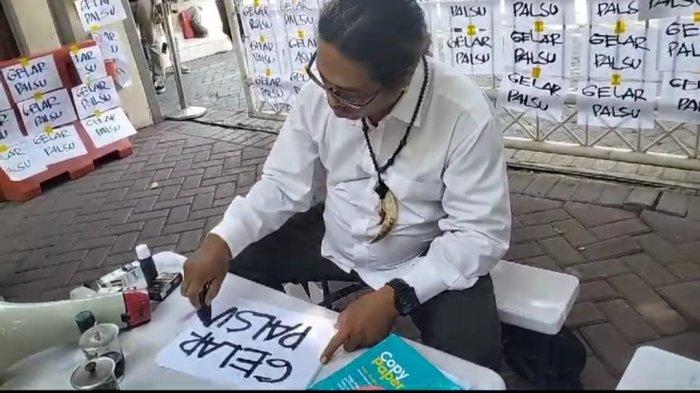 Taufik Monyong, melakukan aksi teatrikal untuk menyoroti kasus gelar palsu.