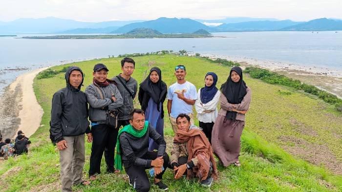 Sejumlah wisatawan berpose dari atas bukit dengan latar pantai dan padang savana Pulau Kenawa, Selasa (31/12/2024).