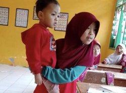 Nuraeni yang masih duduk di bangku kelas dua MI Maddako Sinjai itu menggendong adiknya yang masih kecil di sekolah