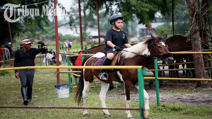 Seorang anak menunggangi kuda ditemani pelatih di Taman Cadika Pramuka Jalan Karya Wisata, Kota Medan, Minggu (23/7). Pemko Medan akan segera merevitalisasi Taman Cadika Pramuka, dan berharap paska revitalisasi, dapat melahirkan atlet-atlet profesional.