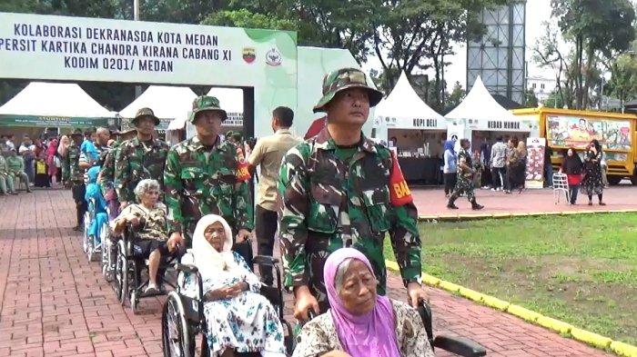 TMMD KODIM MEDAN- Personel TNI-AD sedang mendorong kursi orangtua yang mengikuti bakti sosial. Mereka ditugaskan dalam kegiatan TNI Manunggal Membangun Desa ke-118 tahun 2023 untuk membantu masyarakat.