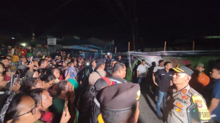 Personel Polres Tanah Karo menenangkan warga yang mulai tidak kondusif saat menyaksikan jalannya rekonstruksi pembakaran rumah Sempurna Pasaribu, di Jalan Nabung Surbakti, Kabanjahe, Jumat (19/7/2024) malam.