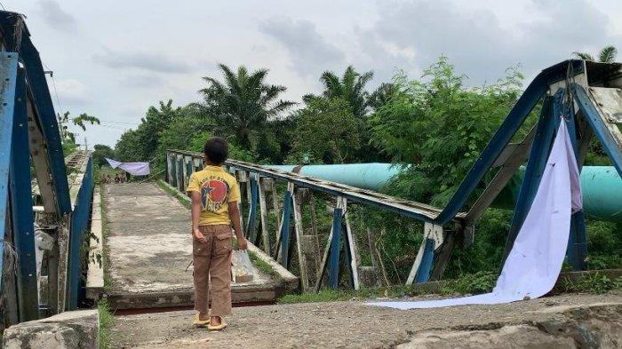 Seorang anak terlihat berjalan di atas jembatan yang roboh di Jalan Pelaksanaan, Desa Bandar Setia, Kecamatan Percut Seituan, Deliserdang, setelah besinya dicuri, Senin (1/7/2024).