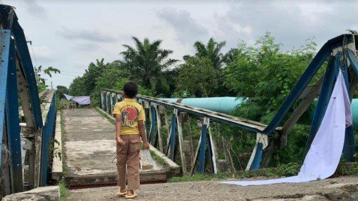 Seorang anak terlihat berjalan di atas jembatan yang roboh di Jalan Pelaksanaan, Desa Bandar Setia, Kecamatan Percut Seituan, Deliserdang, setelah besinya dicuri, Senin (1/7/2024).