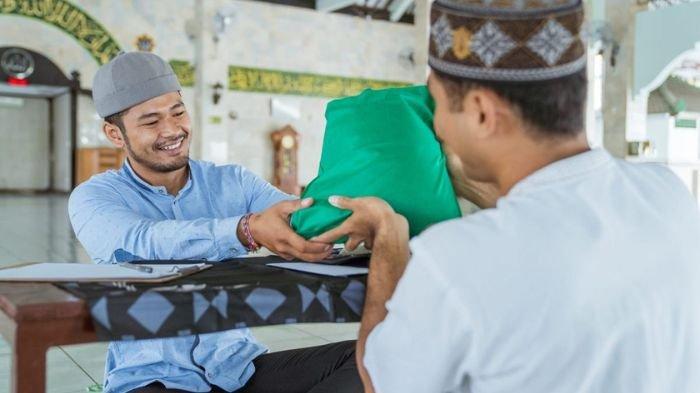 BAYAR ZAKAT- Ilustrasi seorang pria muslim saat tengah membayar zakat fitrah pada panitia pengumpul zakat di sebuah masjid.