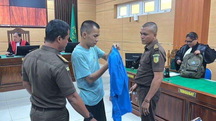 SIDANG KASUS PEMBUNUHAN- Terdakwa In Dragon sedang memasang baju tahanan berwarna biru saat berada di ruang sidang Cakra Pengadilan Negeri Pariaman, Selasa (8/7/2025).