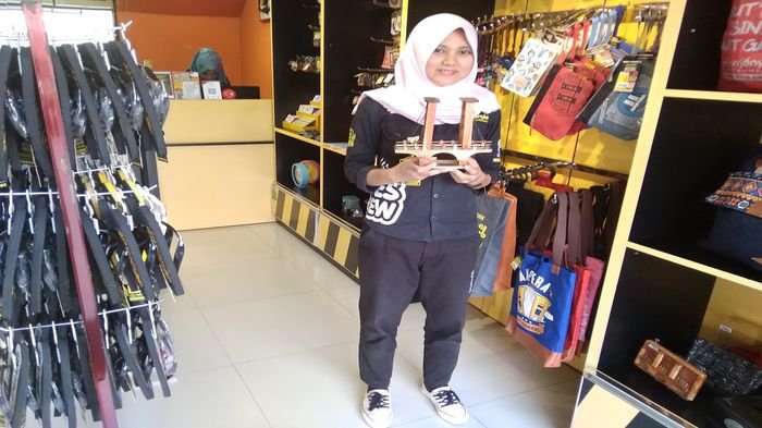 Pramuniaga Outlet Kaos Nyenyes Palembang tengah menunjukkan kaos dan replika jembatan Ampera,