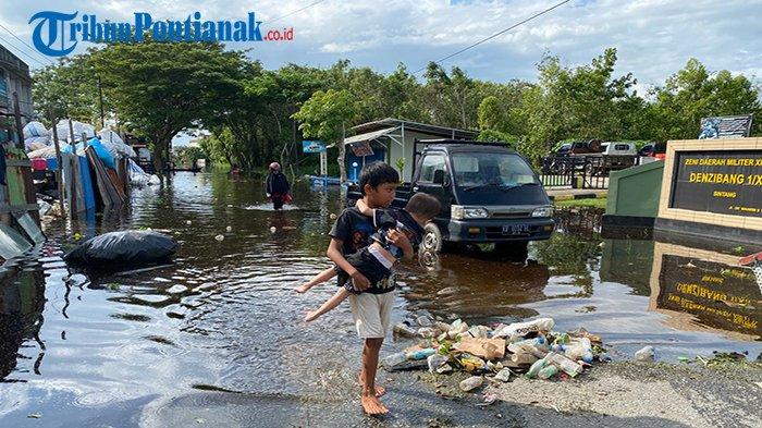 Seorang anak menggendong adiknya melewati jalan yang terendam banjir. Dari pantauan di lapangan, banjir juga merendam jalan pemukiman warga. Ketinggian air bervariasi. Paling dalam lebih dari sepinggang orang dewasa. Sebagian aktivitas warga mulai menggunakan perahu seperti di Jalan Dr Wahidin Sudiro Husodo.