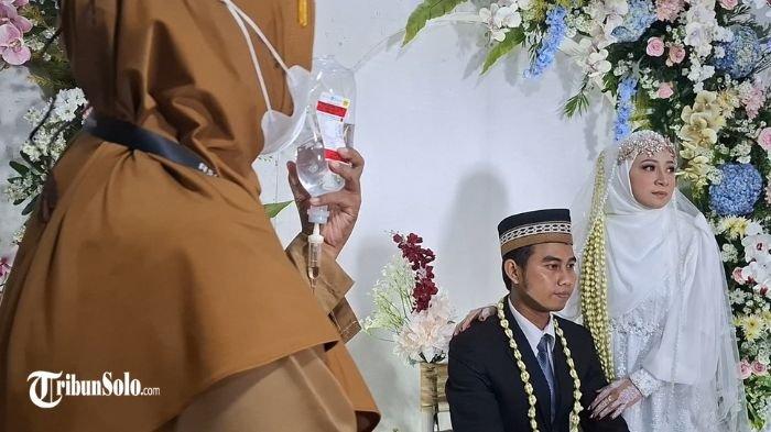 BAHAGIA TAPI LEMAS - Pernikahan Shendy dan Umi warga Kecamatan Sambirejo, Kabupaten Sragen yang melangsungkan pernikahan dalam kondisi sakit di KUA Sambirejo, Sragen, Senin (14/4/2025). Meski nampak gagah dengan balutan setelan jas berwarna hitam, Shendy tidak dapat menyembunyikan kondisinya yang masih lemas. Seorang perawat memegang infus Shendy.