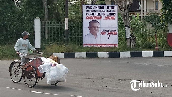 Pengayuh becak melihat ke arah spanduk dukungan Ahmad Luthfi maju Pilkada Jateng 2024