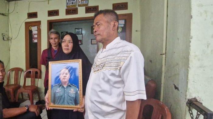 KELUARGA TNI GUGUR MEMEGANG FOTO - Lilis Suryani dan suaminya, Oyib Gunawan, kakak korban Mayor Cpl Anda Rohanda, berada di rumah duka di Kampung Sukasari, Desa Cinunuk, Kecamatan Cileunyi, Kabupaten Bandung, Selasa (13/5/2025).Jenazah Anda akan dibawa ke rumah duka, siang ini.