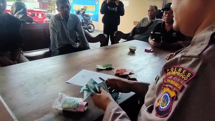 Polisi menghitung uang temuan seorang pemuda saat melintas di jalan simpang empat Kalurahan Pengasih