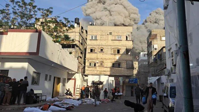 Warga Palestina berlarian mencari tempat berlindung di samping mayat-mayat yang ditutupi setelah serangan udara Israel di dekat Rumah Sakit Kamal Adwan di Beit Lahiya di Jalur Gaza utara pada bulan November 2023