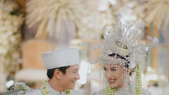 Kedua mempelai yang berbahagia terlihat saling bertatapan. Buku nikah yang selesai ditanda-tangani diletakkan di meja.