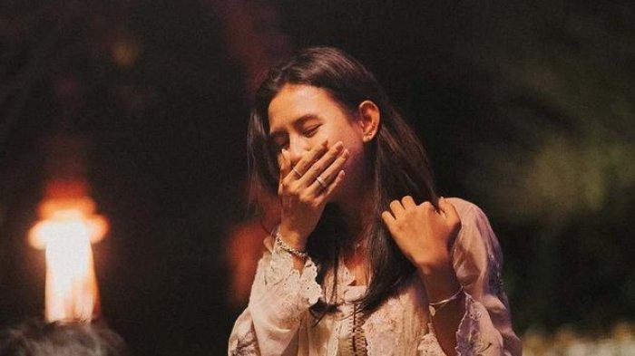 Seperti di film-film, Angga berlutut di hadapan Shenina sambil membawa kotak cincin dan menatapnya dengan penuh keyakinan.