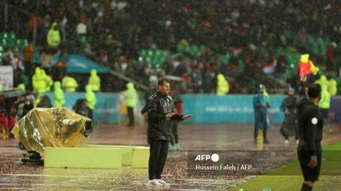 Pelatih raq asal Spanyol Jesus Casas memberi isyarat kepada timnya saat ia berdiri di tengah hujan selama pertandingan sepak bola Piala Teluk Arab antara Irak dan Arab Saudi di Stadion Internasional Basra di kota selatan Irak pada 9 Januari 2023. Hussein Faleh / AFP