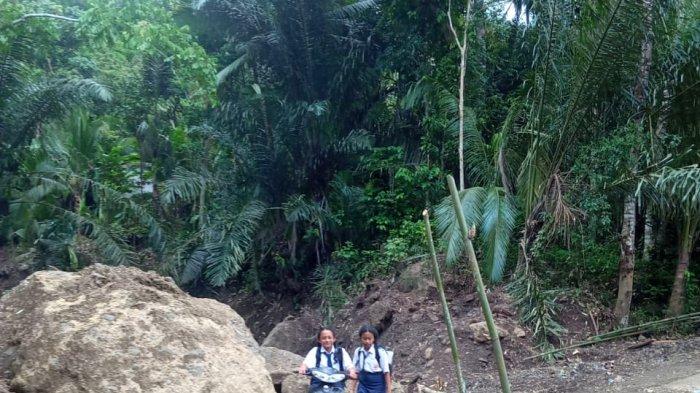 MELINTASI JALAN - Siswa di Banjar Kalanganyar, Desa Gegelang, Kecamatan Manggis, Karangasem saat hendak melewati jalan rusak, Senin (29/4). Jalan pelintas tergerus akibat banjir bandang dan longsor. 