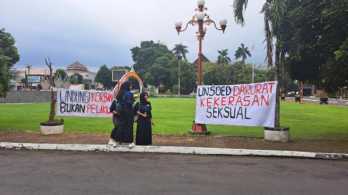 MAHASISWA LAWAN KEKERASAN - Sejumlah mahasiswa membentangkan spanduk protes di depan Gedung Rektorat Unsoed, Purwokerto, Rabu (23/7/2025), untuk menyuarakan keprihatinan atas kasus dugaan kekerasan atau pelecehan seksual oleh oknum guru besar. Aksi ini dilakukan dengan cara menuliskan tuntutan tegas pada spanduk, mendesak Unsoed untuk melindungi korban dan tidak menutupi kasus yang diduga melibatkan seorang profesor FISIP tersebut. 