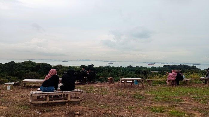 Warga Batam duduk-duduk di spot wisata Bukit Harimau Sekupang, menikmati pemandangan pantai dan gedung pencakar langit Singapura.