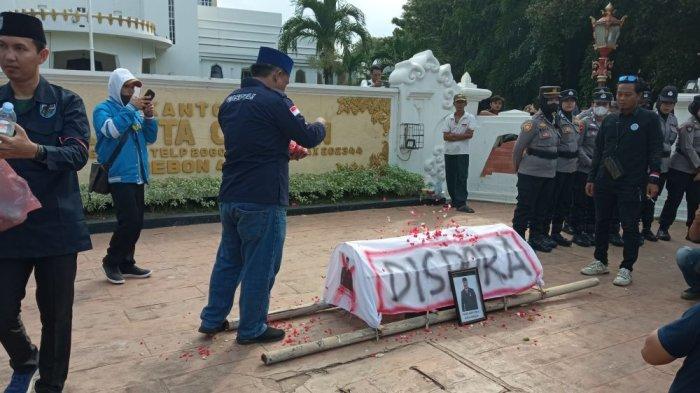 PULUHAN PEMUDA DEMO - Keranda bertuliskan Dispora menjadi salah satu alat peraga puluhan pemuda yang tergabung dalam Komite Nasional Pemuda Indonesia (KNPI) Kota Cirebon menggelar aksi unjuk rasa di depan Balai Kota Cirebon, Jumat (2/5/2025) siang