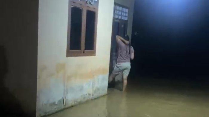 Seorang warga terekam di depan rumah yang sudah terendam banjir.