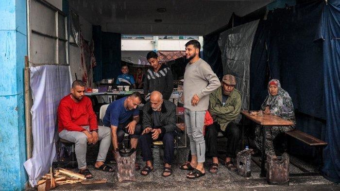 Orang-orang berlindung dari hujan di aula yang menghadap ke halaman sekolah yang dikelola oleh Badan Bantuan dan Pekerjaan PBB untuk Pengungsi Palestina di Timur Dekat