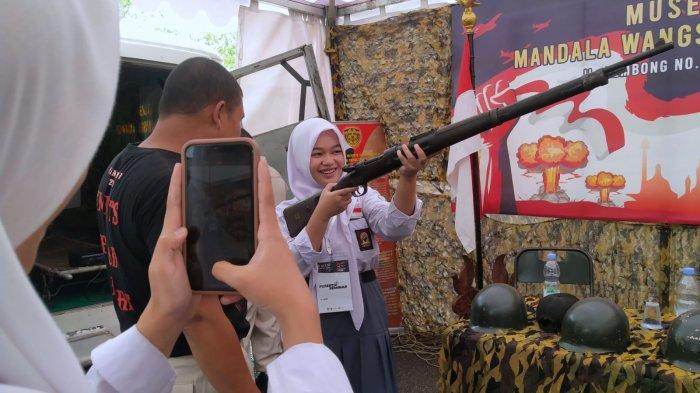 Pelajar berfoto sambil memegang senjata yang digunakan pada masa penjajahan koleksi Museum Mandala Wangsit dalam gelaran Museum Monpera Expo di pelataran Moseum Perjuangan Rakyat Jawa Barat (Monpera Jabar), Jalan Dipatiukur, Kota Bandung, Jawa Barat, Kamis (2/11/2023).