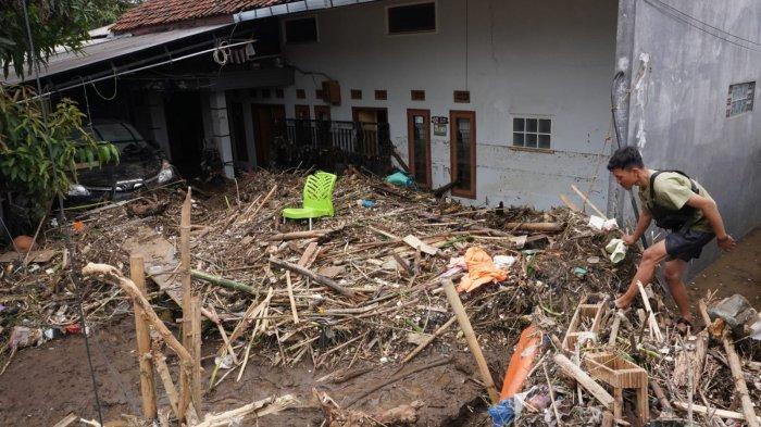 Warga melintasi satu rumah dan mobil yang terparkir di garasi tertimbun lumpur dan material sampah di sekitar lokasi tanggul Sungai Cigede yang jebol, di Kampung Lamajang Peuntas, Desa Citeureup, Kecamatan Dayeuhkolot, Kabupaten Bandung, Jawa Barat, Jumat (12/1/2024).