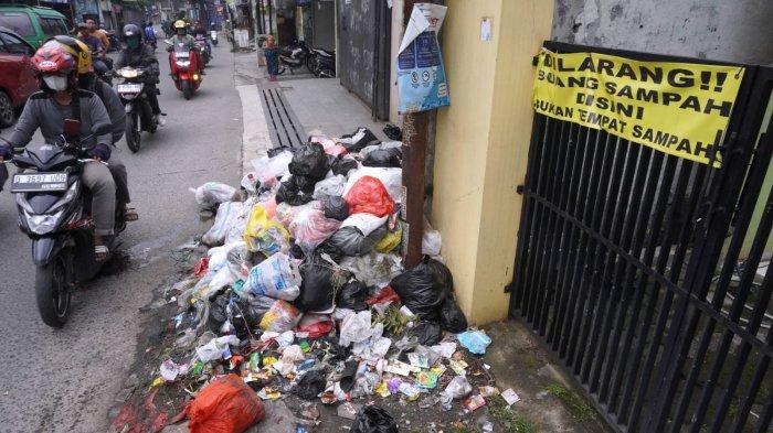 Pengguna jalan melintasi sampah yang sudah menumpuk di depan salah satu rumah di pinggir Jalan Sayuran, Desa Cangkuang Kulon, Kecamatan Dayeuhkolot, Kabupaten Bandung, Jawa Barat, Jumat (26/4/2024).