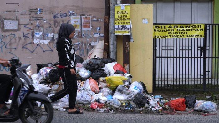 Pengguna jalan melintasi sampah yang sudah menumpuk di depan salah satu rumah di pinggir Jalan Sayuran, Desa Cangkuang Kulon, Kecamatan Dayeuhkolot, Kabupaten Bandung, Jawa Barat, Jumat (26/4/2024).