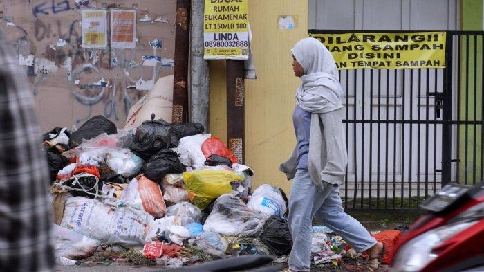 Pengguna jalan melintasi sampah yang sudah menumpuk di depan salah satu rumah di pinggir Jalan Sayuran, Desa Cangkuang Kulon, Kecamatan Dayeuhkolot, Kabupaten Bandung, Jawa Barat, Jumat (26/4/2024).