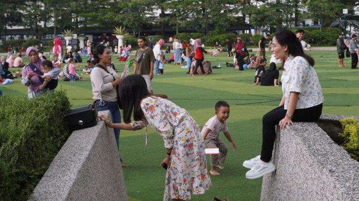 Pengunjung berfoto menggunakan ponsel di pinggiran lapangan rumput sintetis Taman Alun-Alun Kota Bandung, Jawa Barat, Kamis (9/5/2024).