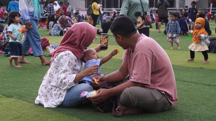 Pengunjung berswafoto sambil bersantai di lapangan rumput sintetis Taman Alun-Alun Kota Bandung, Jawa Barat, Kamis (9/5/2024).