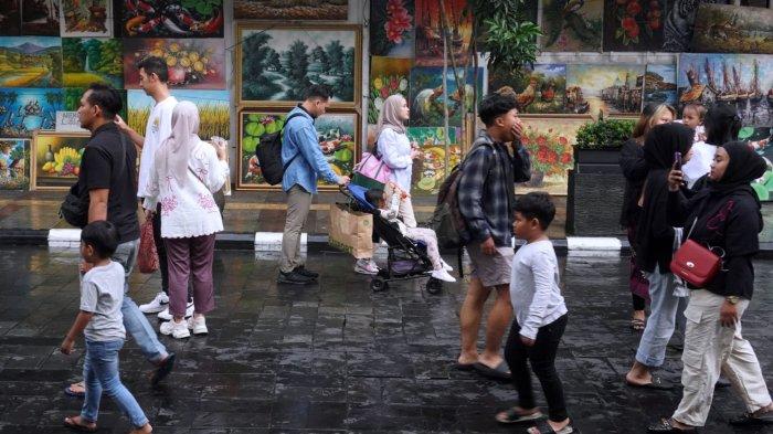 Wisatawan melintasi sejumlah lukisan yang dipajang di trotoar saat jalan-jalan sore bebas kendaraan (Braga Free Vehicle) di Jalan Braga, Kota Bandung, Jawa Barat, Sabtu (18/5/2024).
