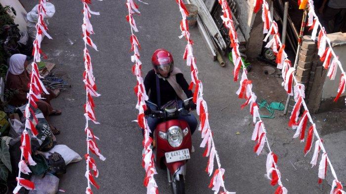 Pengendara sepeda motor melintas di Jalan Kampung Mengger Hilir yang dihiasi rarawisan merah putih, di RW 03, Kampung Mengger Hilir, Desa Sukapura, Kecamatan Dayeuhkolot Kabupaten Bandung, Sabtu (10/8/2024).