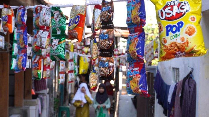 Warga melintas di salah satu gang yang dihiasi kemasan berisi makanan kadaluarsa, di RW 03, Kampung Mengger Hilir, Desa Sukapura, Kecamatan Dayeuhkolot Kabupaten Bandung, Sabtu (10/8/2024).